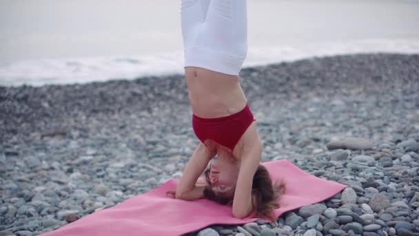 Kadın denize yakın çakıl plaj üzerinde amuda kalkma performans, Hatha Yoga uygulama — Stok video