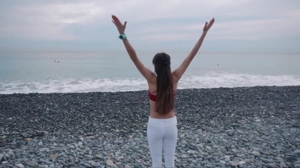 上午, 女运动员独自站在鹅卵石海滩上伸展身体 — 图库视频影像