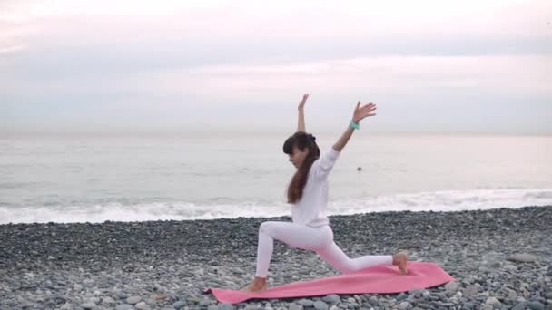 Woman is relaxing in yoga asanas on pebble sea shore in morning time — Stock Video