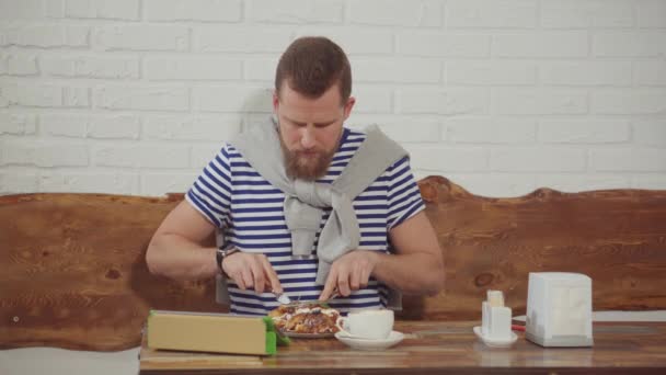 El hombre está escribiendo en la tableta en la cafetería y comer postre con café — Vídeo de stock