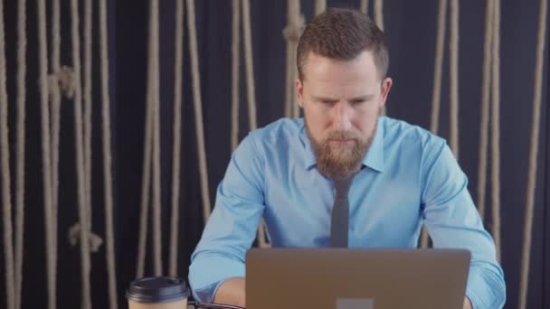 Männliche Büroangestellte blickt konzentriert auf das Display ihres Laptops und lehnt sich zurück — Stockvideo