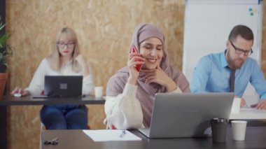 Genç Müslüman kadın modern ofis odasında cep telefonu tarafından konuşuyor