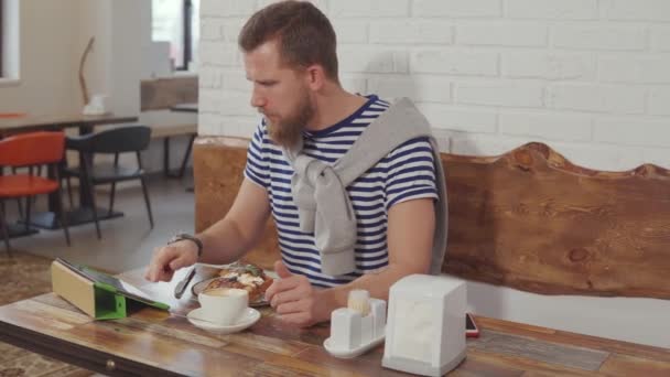 男はデザートを食べて、カフェでウェブをサーフィン. — ストック動画