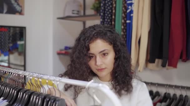 Жінка купує в магазині одягу в торговому центрі, беручи вішалки зі стійки — стокове відео