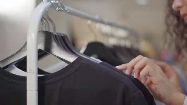 Mujer está buscando camiseta en el estante en la tienda de ropa, primer plano de sus manos — Vídeos de Stock