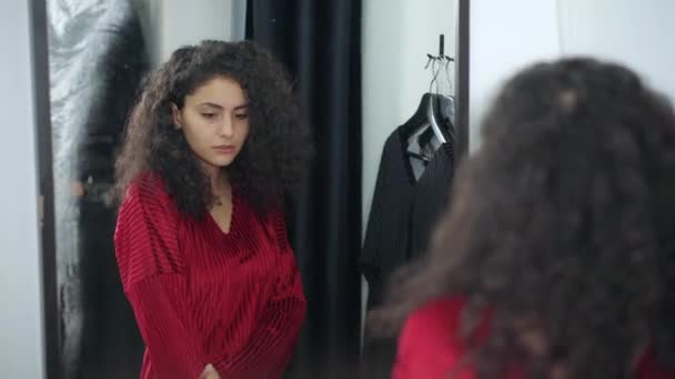 Teenagermädchen sieht sich selbst im Spiegel im Geschäft an, gekleidet in rotes Kleid — Stockvideo