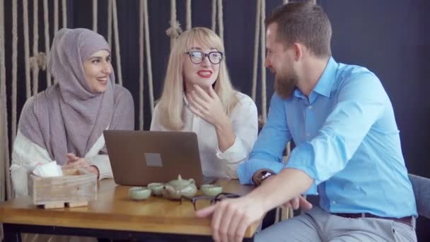 Мужчина рассказывает забавную историю двум своим подружкам в кафе, смеющимся вместе — стоковое видео