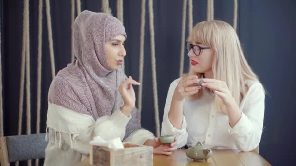 Två muslimska och kaukasiska kvinnor chattar sitter i kafé och dricker te — Stockvideo