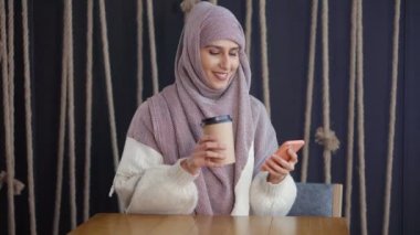Arap kadın akıllı telefonda SMS yazarak, kahve karton ile kafede oturuyor