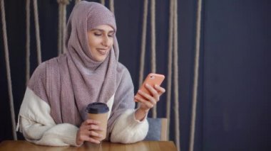 Yetişkin neşeli Müslüman kadın cep telefonu SMS okuma ve kafede gülümsüyor