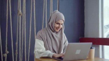 Mutlu Müslüman kadın ücretsiz WiFi ile kafede dizüstü bilgisayar ile online sohbet ediyor