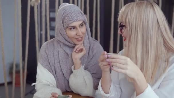 アラビアの女性はお茶を飲むときに彼女のブロンドの女性の友人に秘密を話している — ストック動画