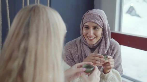 Mujer árabe alegre está escuchando la historia de su amiga rubia en la cafetería — Vídeo de stock