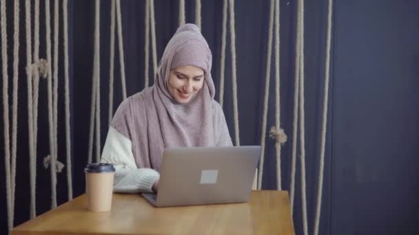 Alegre dama musulmana está leyendo mensajes en el cuaderno, sonriendo y escribiendo respuesta — Vídeos de Stock