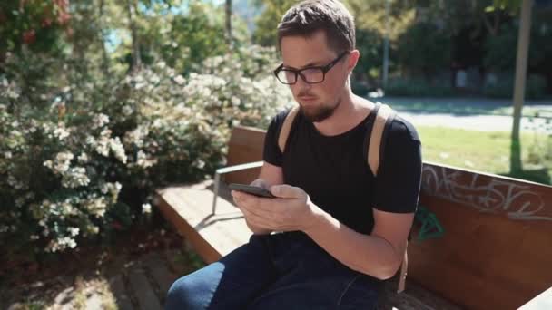 Einsamer männlicher Tourist schaut auf Bildschirm seines Smartphones, sitzt im Park — Stockvideo