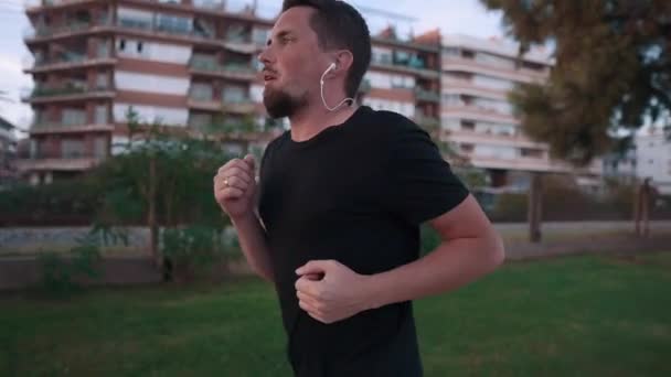 Guy está ouvindo música por fones de ouvido e jogador durante a corrida da noite ao ar livre — Vídeo de Stock