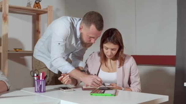 Женщина консультируется со своим менеджером в офисе, он рисует в ее блокноте — стоковое видео