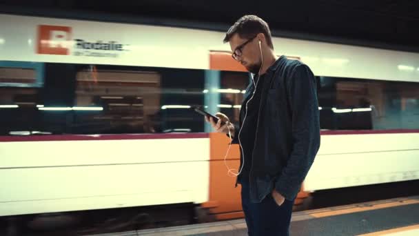 Barcelona, Spanien September 2018. Manliga turist med smartphone som lyssnar på musik i hörlurar i väntan på ett tåg i Barcelona Metropolitan. — Stockvideo