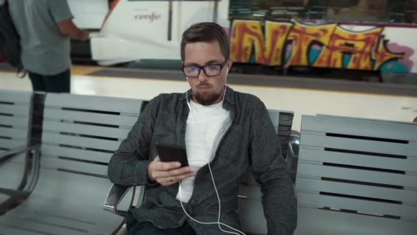 Barcelona, España Septiembre 2018. Hombre con gafas sentado en un banco de surf web en el teléfono inteligente en el metro de Barcelona. Nuevo tren al llegar a la estación de Barcelona Metropolitan . — Vídeos de Stock