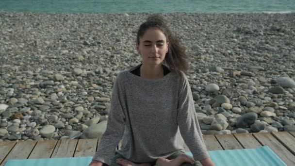 Jeune femme mince est relaxant assis dans lotus asana sur la côte de la mer — Video