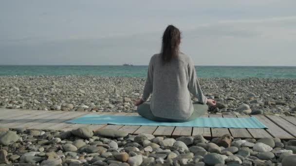 Mujer atleta solitaria está disfrutando de la vista sobre el paisaje marino, sentado piernas cruzadas en la playa — Vídeos de Stock