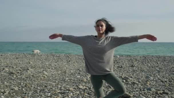 Femme athlétique est debout sur une jambe et levant les mains contre le paysage marin — Video