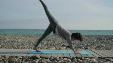 Kadın elleriyle yere eğiliyor ve bacağını kaldırıyor, dışarıda yoga yapıyor.