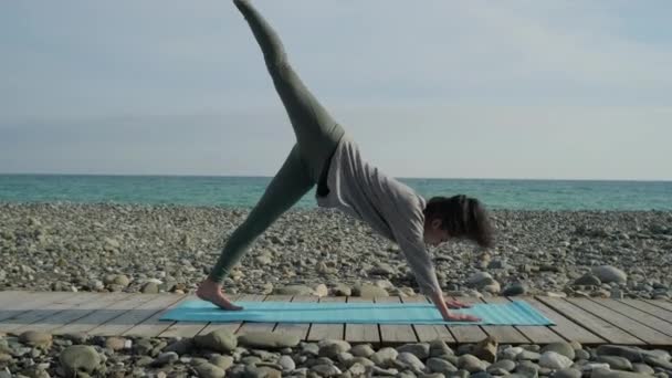 Kadın elleriyle yere eğiliyor ve bacağını kaldırıyor, dışarıda yoga yapıyor. — Stok video