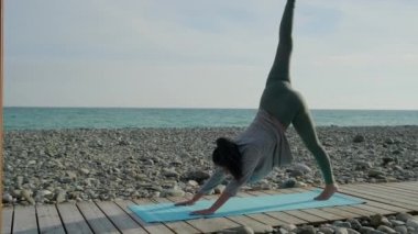 Genç sporcu kadın güneşli bir günde yoga dersinde vücudunu esnetiyor.