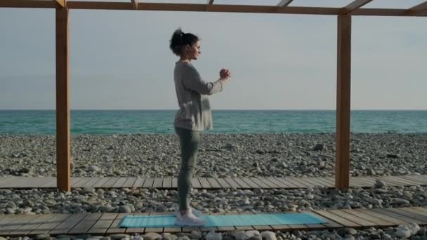 Дівчина брюнетка тренування м'язів ніг і сідниць, сидячи в морському узбережжі — стокове відео