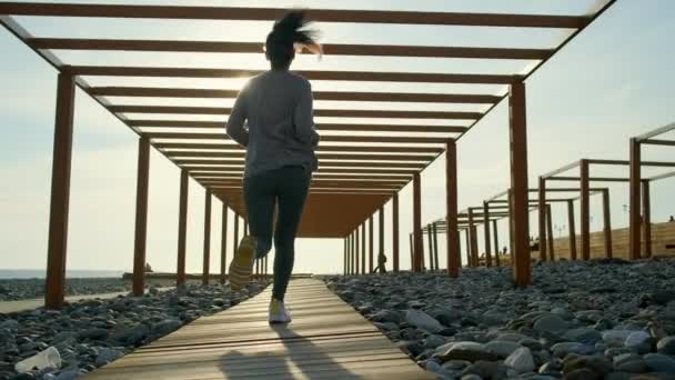 Chica atlética delgada está corriendo sobre camino de madera en terraplén, vista desde el suelo — Vídeo de stock