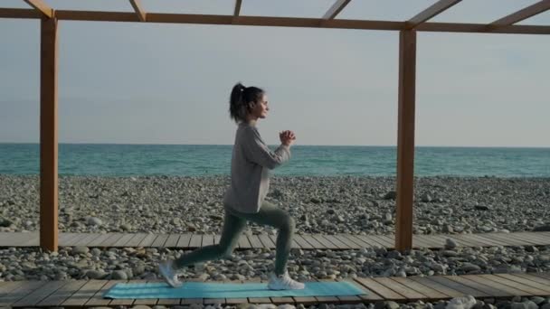 La mujer está haciendo embestidas y agachándose al aire libre, entrenando su cuerpo — Vídeos de Stock