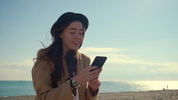 Adolescente está leyendo noticias en la red social en el móvil y sonriendo en la playa — Vídeos de Stock