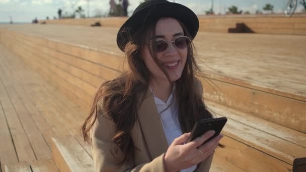 Menina feliz romântico está lendo sms em seu smartphone, senta-se ao ar livre em dia ensolarado — Vídeo de Stock