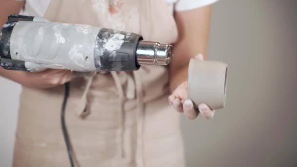 陶芸家の女性は、テクニカルドライヤー、クローズアップによってセラミックカップに熱い空気を吹いています — ストック動画