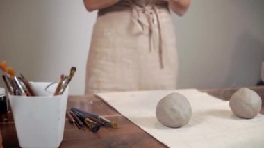 Kadın usta çalışma stüdyosunda kil yoğurıyor, masanın yanında duruyor