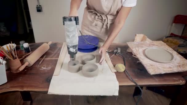 Potter vrouw is drogen door hete luchtpistool rauwe keramische servies in workshop — Stockvideo