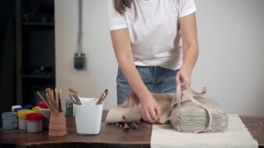 Kadın el işi atölyesinde önlük takıyor, masanın yanında duruyor.,