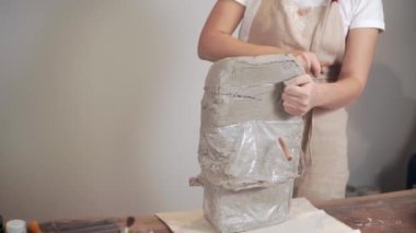 Kadın heykeltıraş stüdyoda metal tel ile ıslak kil büyük parça kesiyor