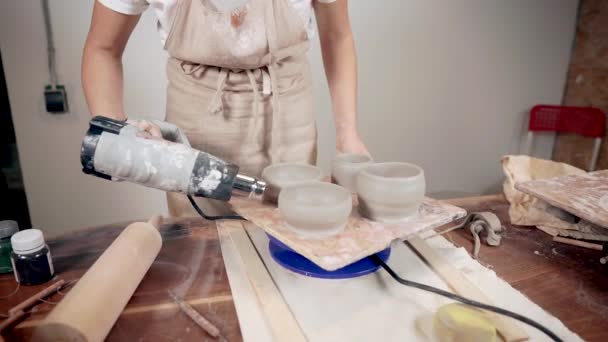 Kobieta artysta wieje przez pistolet gorącego powietrza na miski ceramiczne w warsztacie — Wideo stockowe