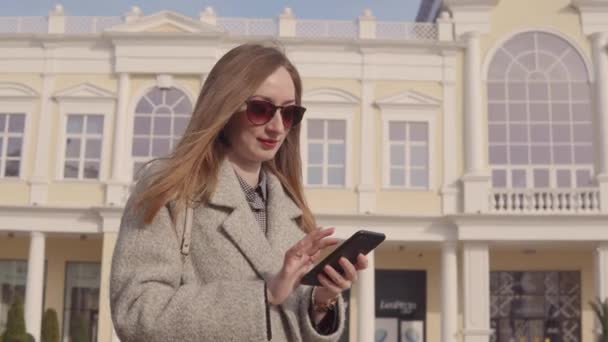 Mujer Smilimg mensajes de texto en el teléfono inteligente al aire libre . — Vídeos de Stock