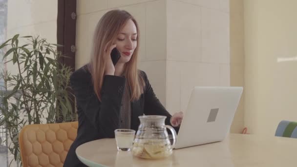 Felnőtt nő beszél a mobil telefon és gépelés-ra notebook az irodájában — Stock videók