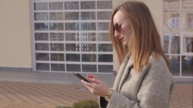 Yetişkin lüks kadın şehirde sokakta akıllı telefon ile SMS gönderiyor, bahar günü
