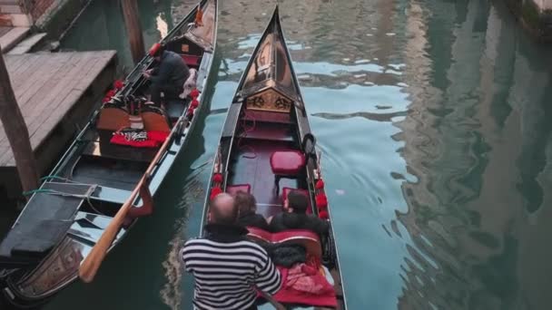 Италия, Венеция - февраль 2019 года: Гондола с двумя путешественниками и гондольером плывет, вид с моста — стоковое видео