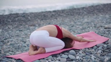 Genç bir kadın spor kıyafetleriyle plajda yoga yapıyor..