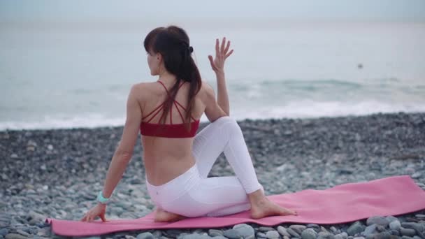 Mujer estirándose al aire libre en la playa en una alfombra . — Vídeos de Stock