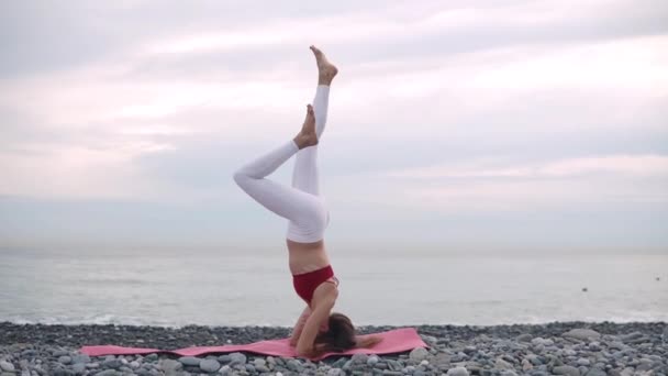 Γυναίκα κάνει headstand στην παραλία στο στρώμα γιόγκα. — Αρχείο Βίντεο