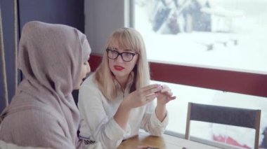 İki gülen kadın bir kafede vakit geçiriyor.