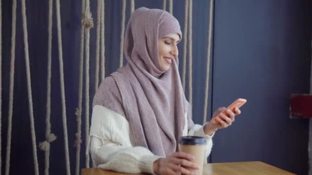 Chica musulmana en un café con un teléfono inteligente — Vídeos de Stock