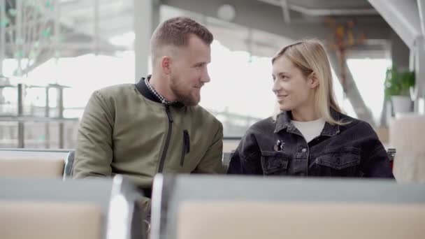 Pár cestovatelů mluví, sedí v čekárně na letišti, muž a dívka, — Stock video